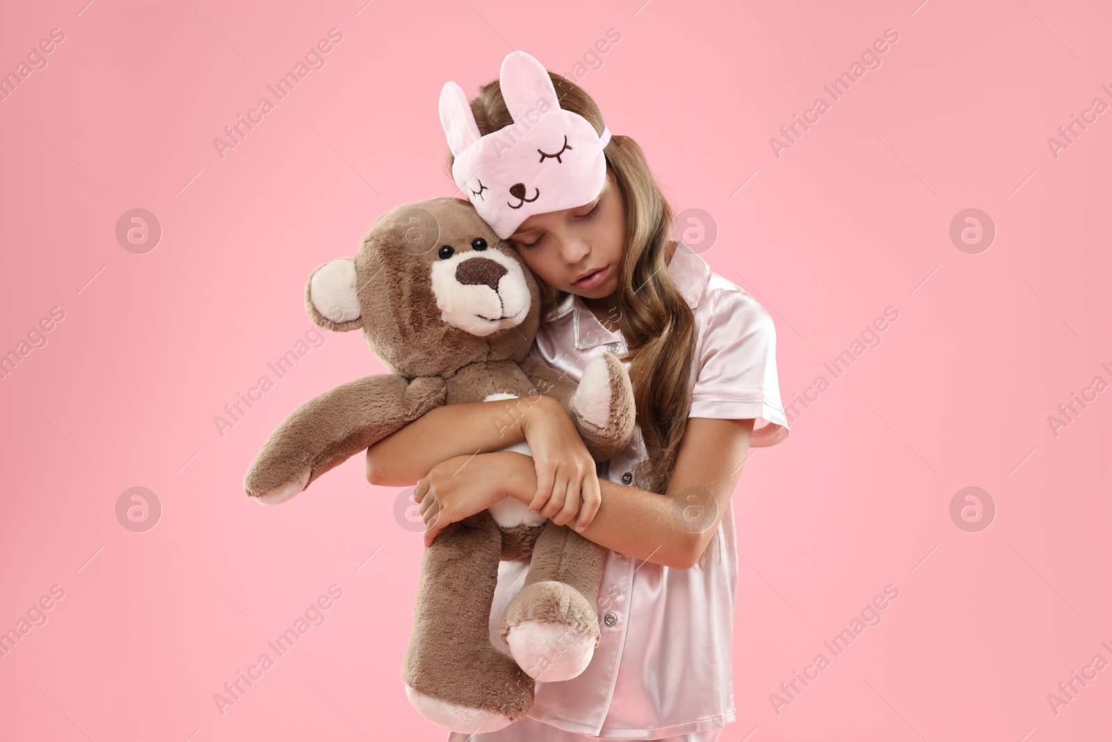 Photo of Overslept girl with sleep mask and teddy bear on pink background