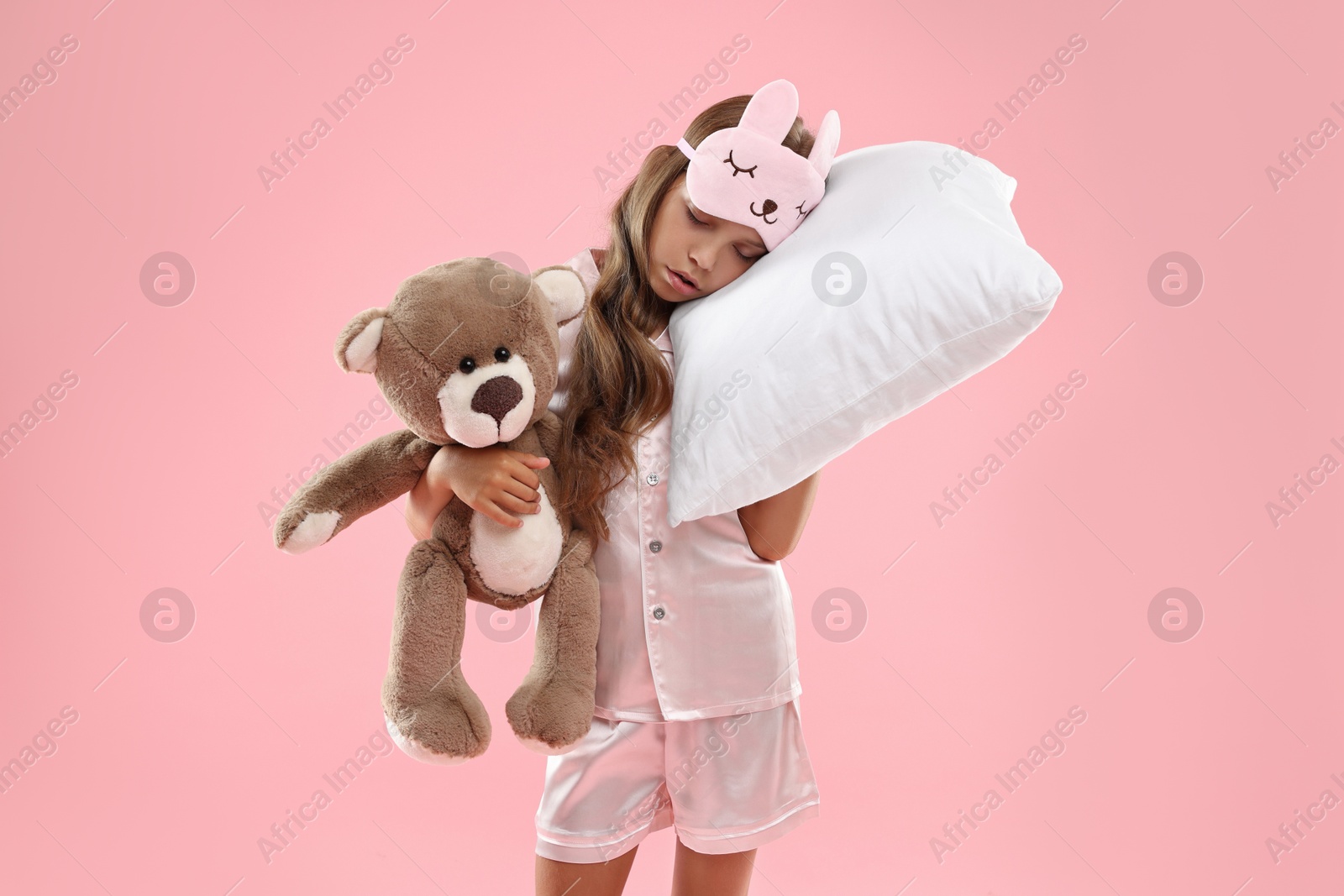 Photo of Overslept girl with sleep mask, pillow and teddy bear on pink background