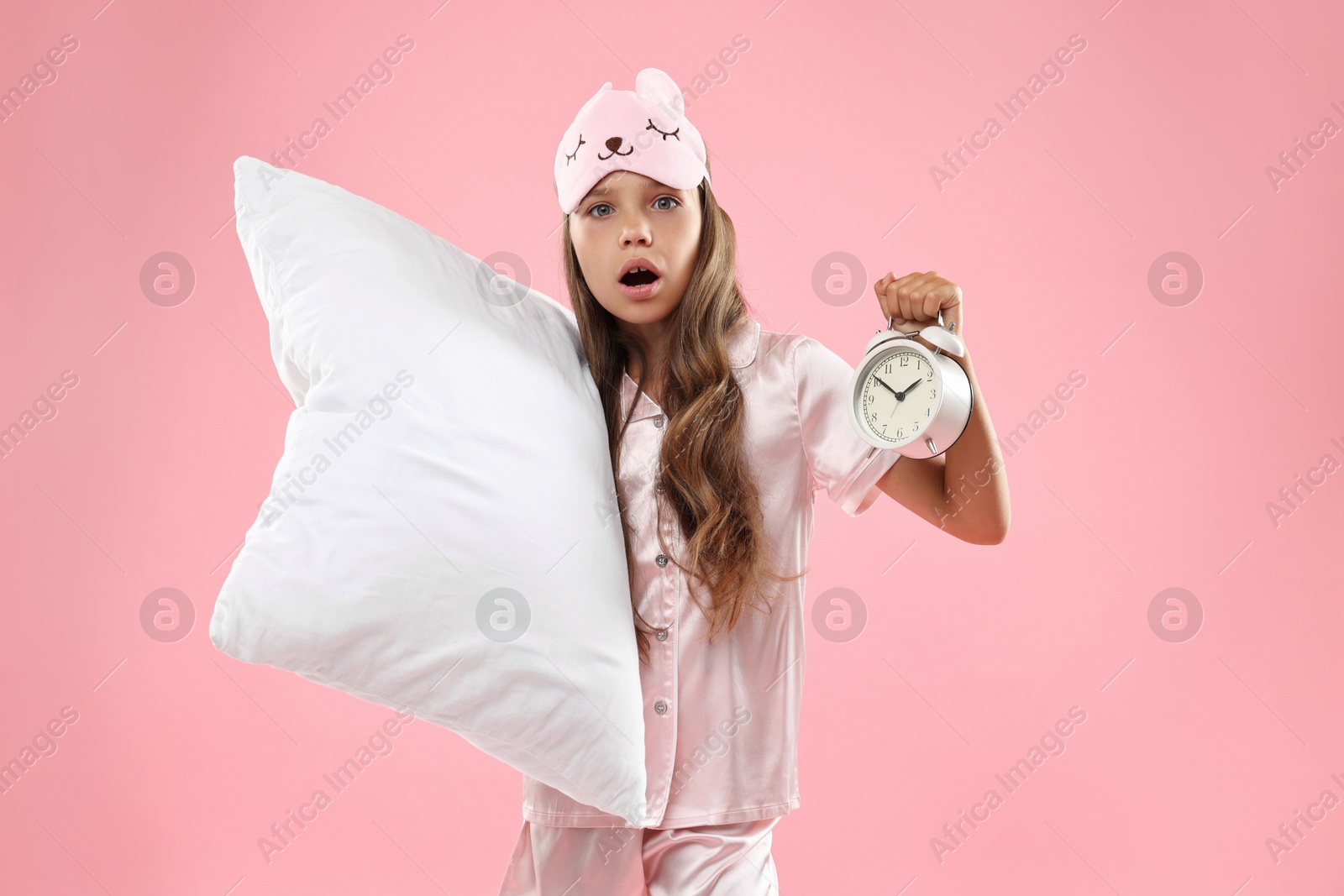 Photo of Overslept girl with sleep mask, pillow and alarm clock on pink background