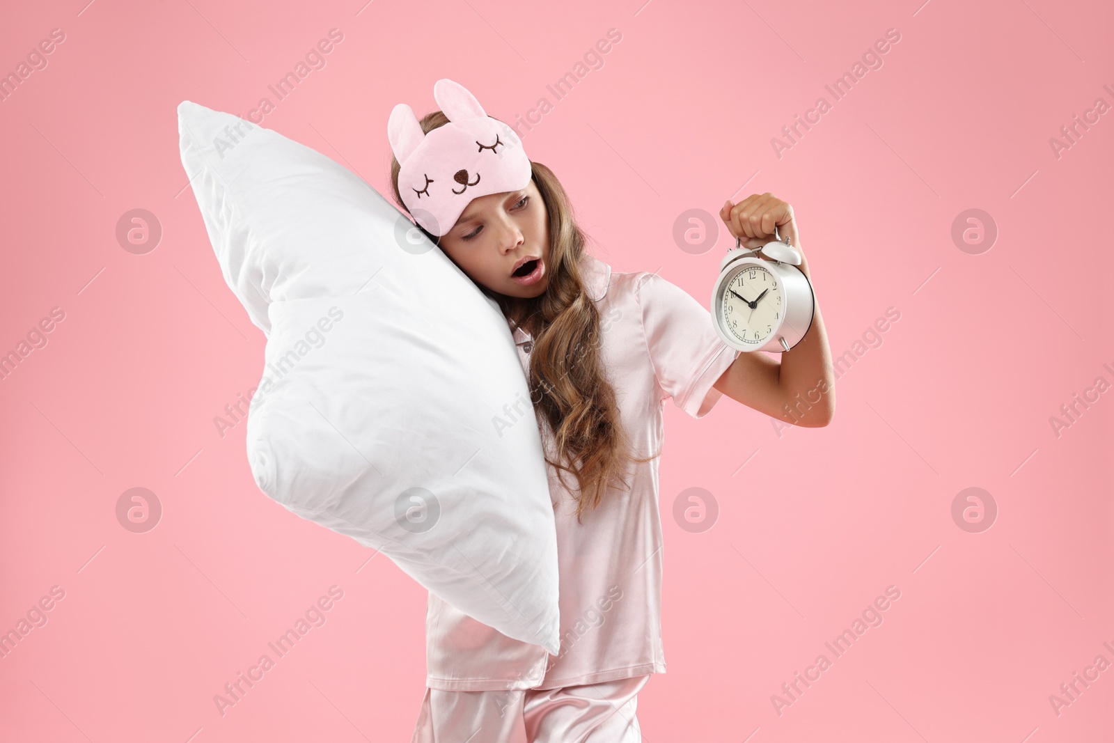 Photo of Overslept girl with sleep mask, pillow and alarm clock on pink background