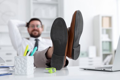 Businessman holding legs on table in office, selective focus. Break time