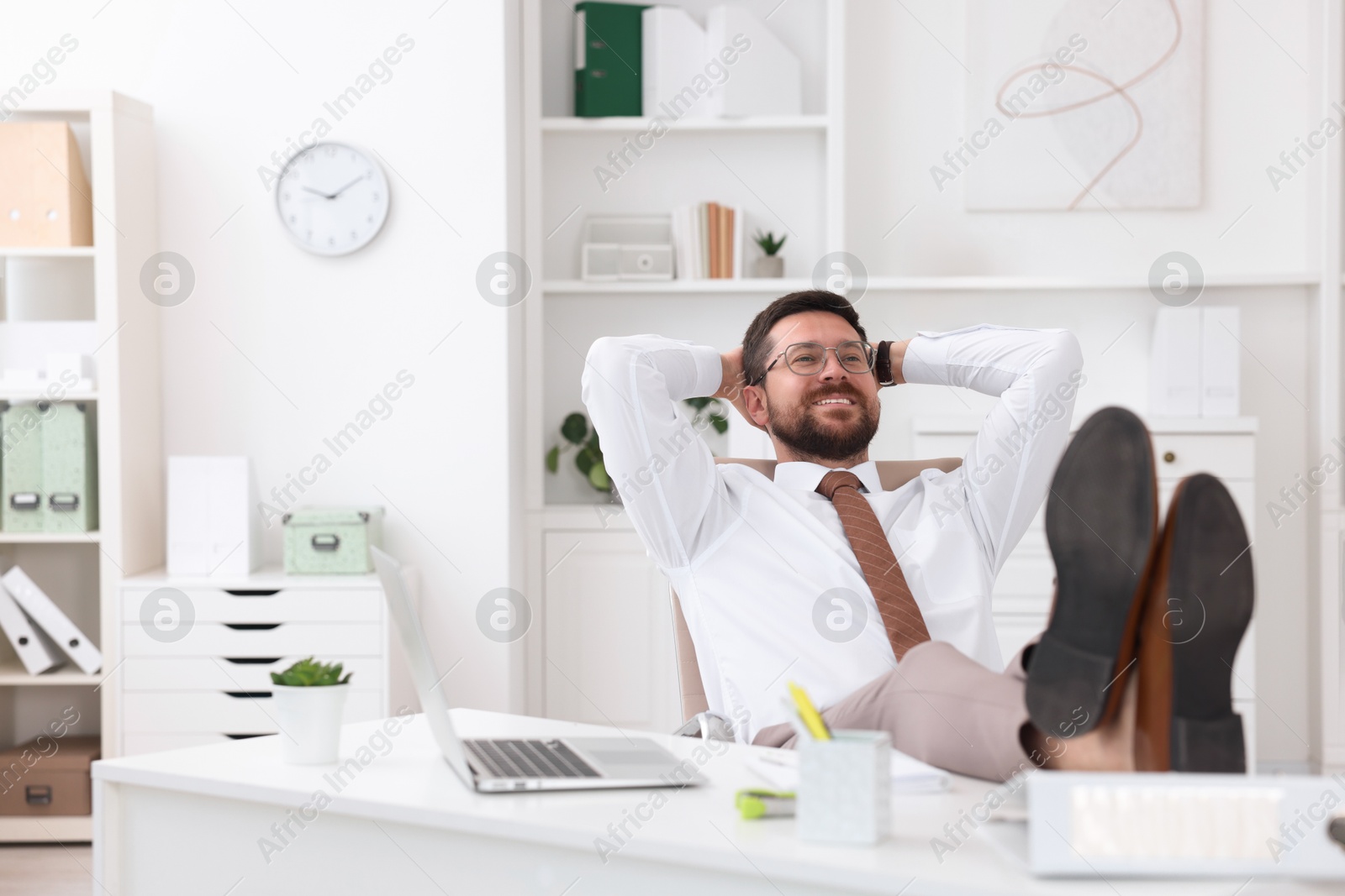 Photo of Smiling businessman with hands behind his head holding legs on table in office. Break time