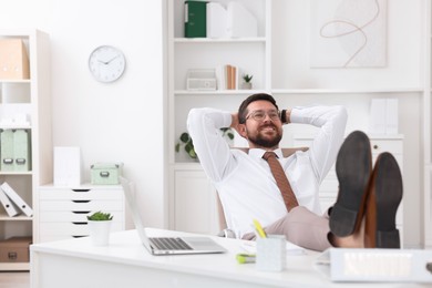 Smiling businessman with hands behind his head holding legs on table in office. Break time