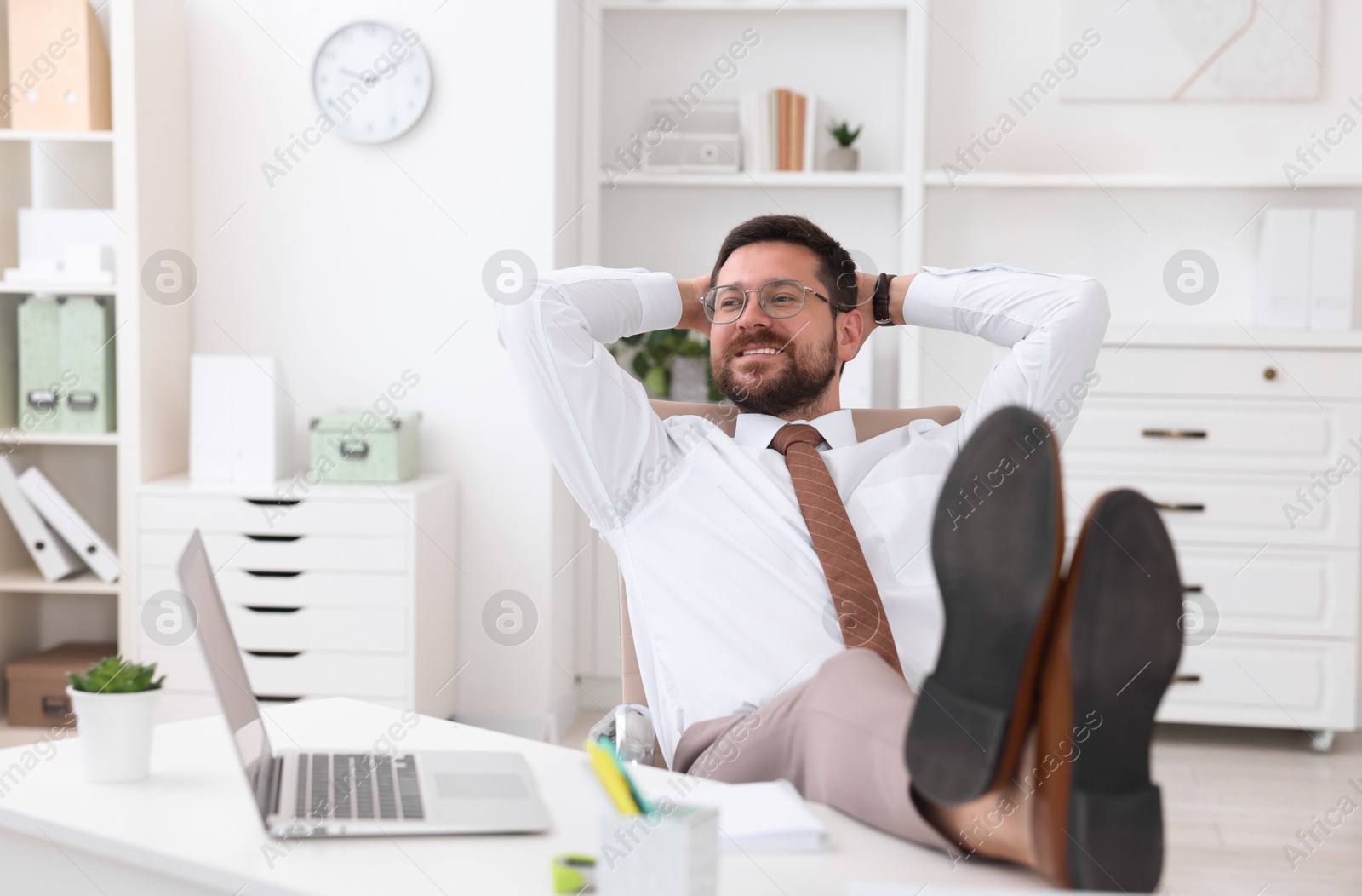 Photo of Smiling businessman with hands behind his head holding legs on table in office. Break time