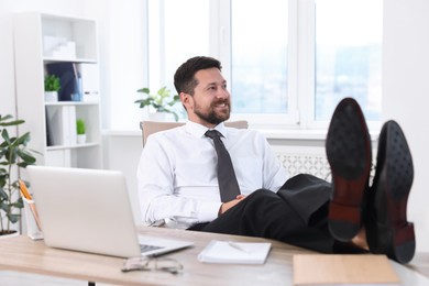 Smiling businessman holding legs on table in office. Break time