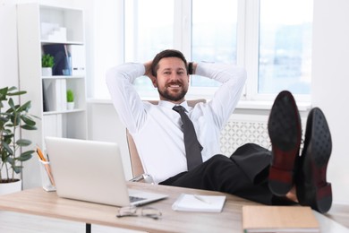 Smiling businessman with hands behind his head holding legs on table in office. Break time