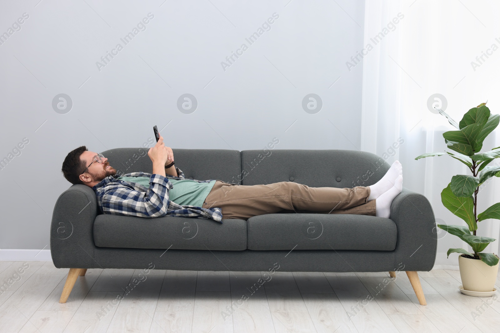 Photo of Smiling man with smartphone relaxing on sofa at home