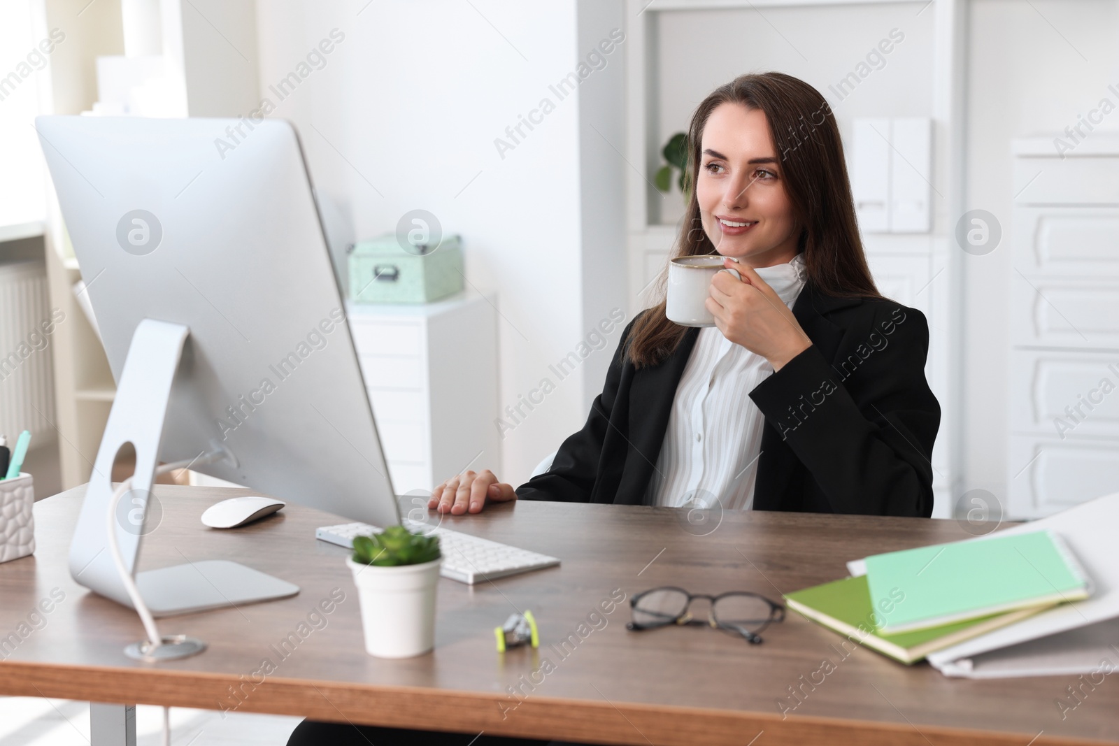 Photo of Smiling businesswoman drinking coffee at table in office. Break time