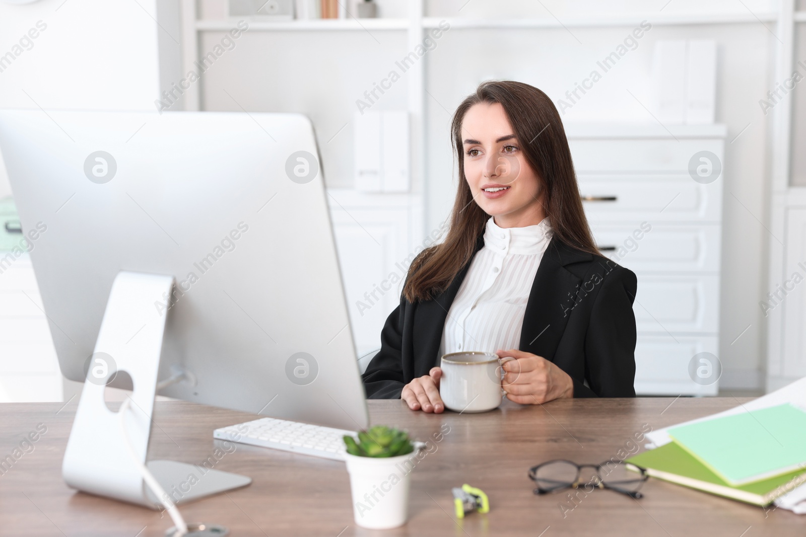 Photo of Smiling businesswoman drinking coffee at table in office. Break time