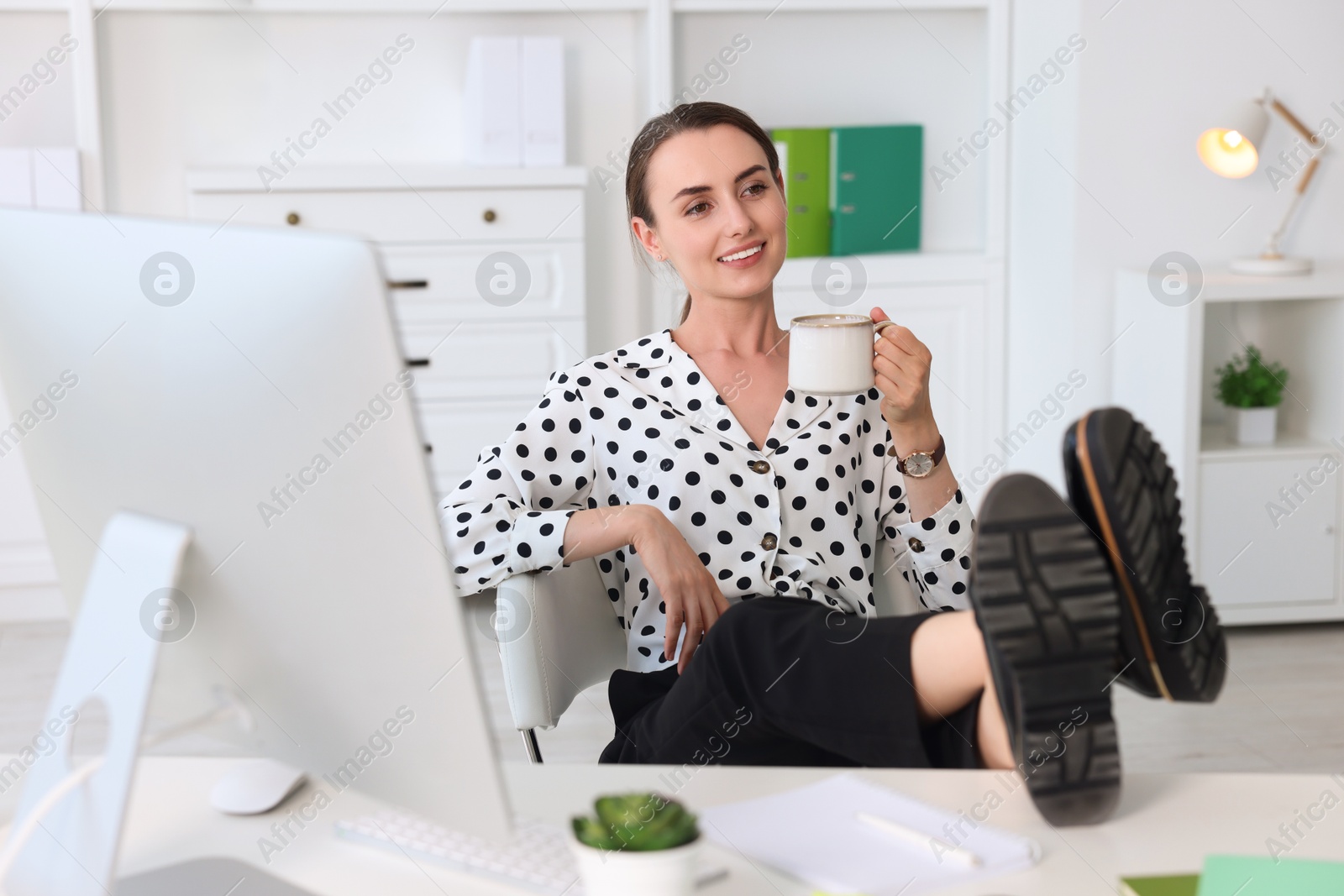 Photo of Smiling businesswoman drinking coffee holding legs on table in office. Break time