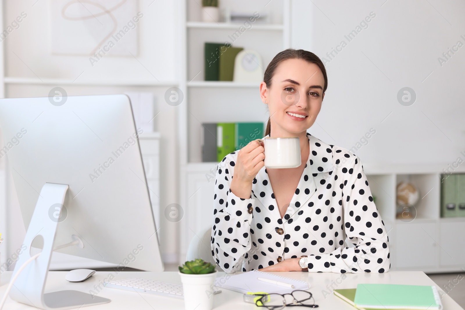 Photo of Smiling businesswoman drinking coffee at table in office. Break time