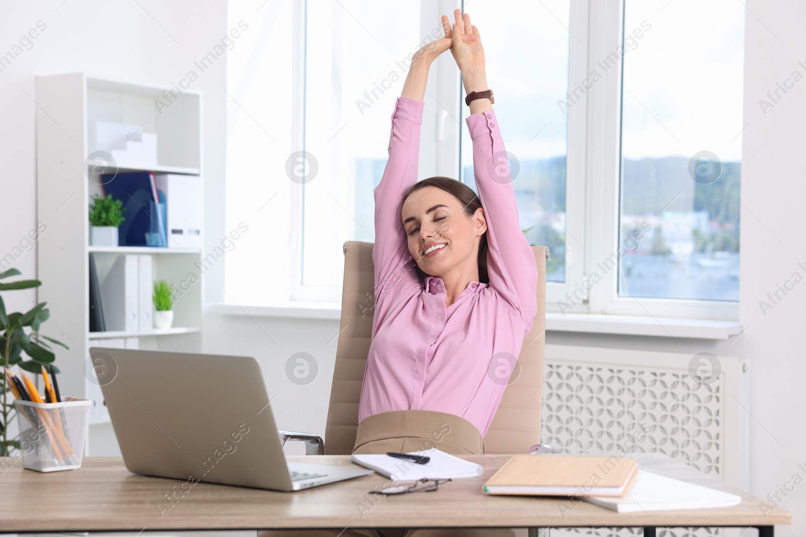 Photo of Smiling businesswoman stretching at table in office. Break time