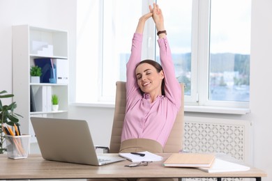 Smiling businesswoman stretching at table in office. Break time