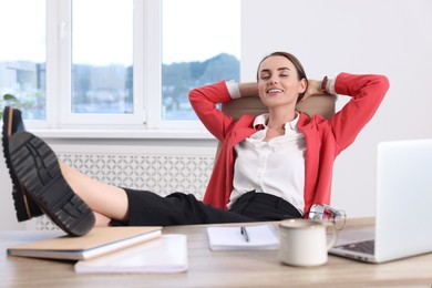 Smiling businesswoman with hands behind her head holding legs on table in office. Break time