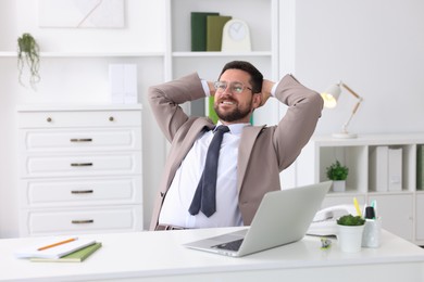 Photo of Smiling businessman with hands behind his head at table in office. Break time