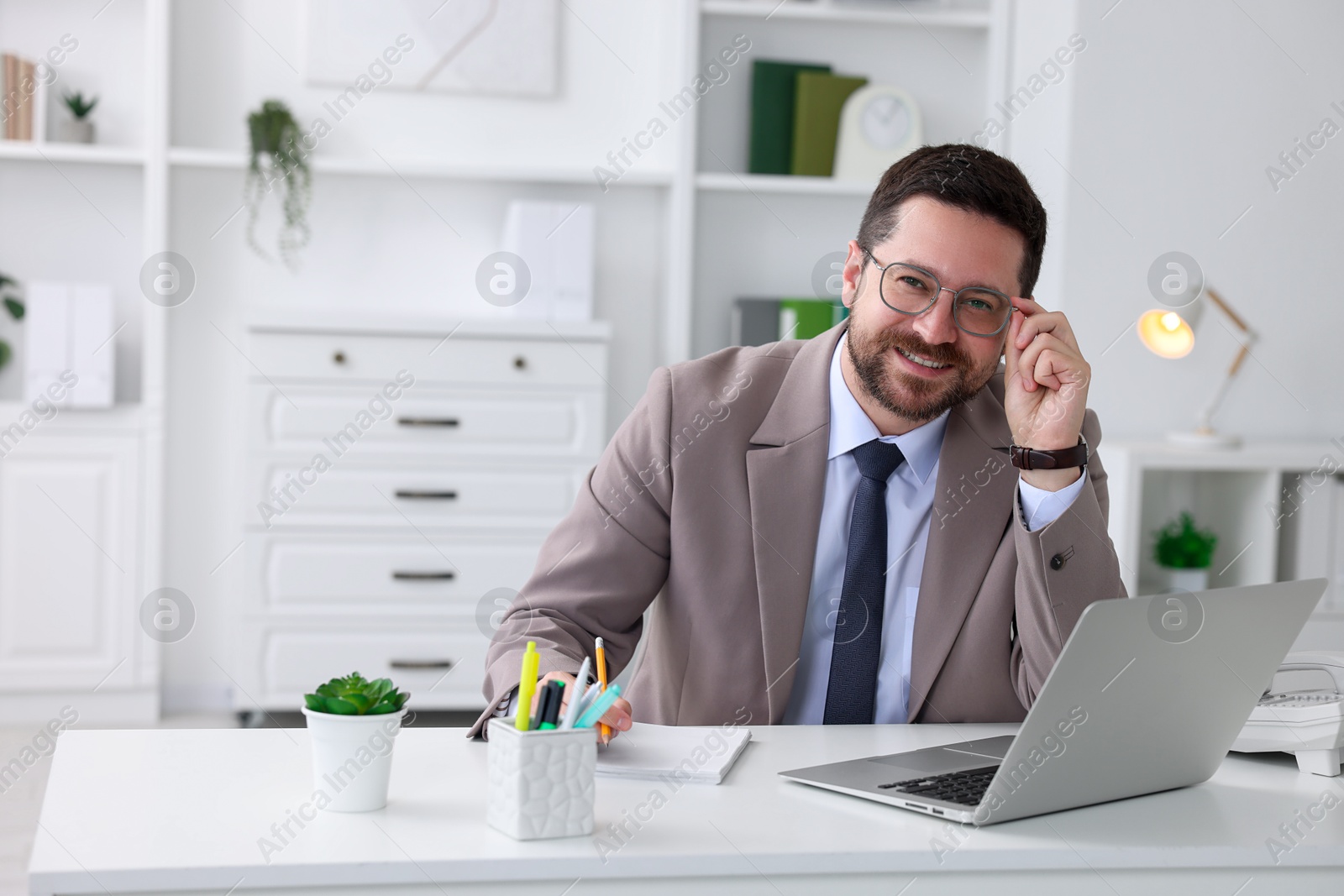 Photo of Portrait of smiling businessman at table in office. Space for text