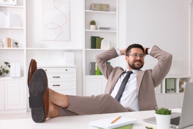 Smiling businessman with hands behind his head holding legs on table in office. Break time