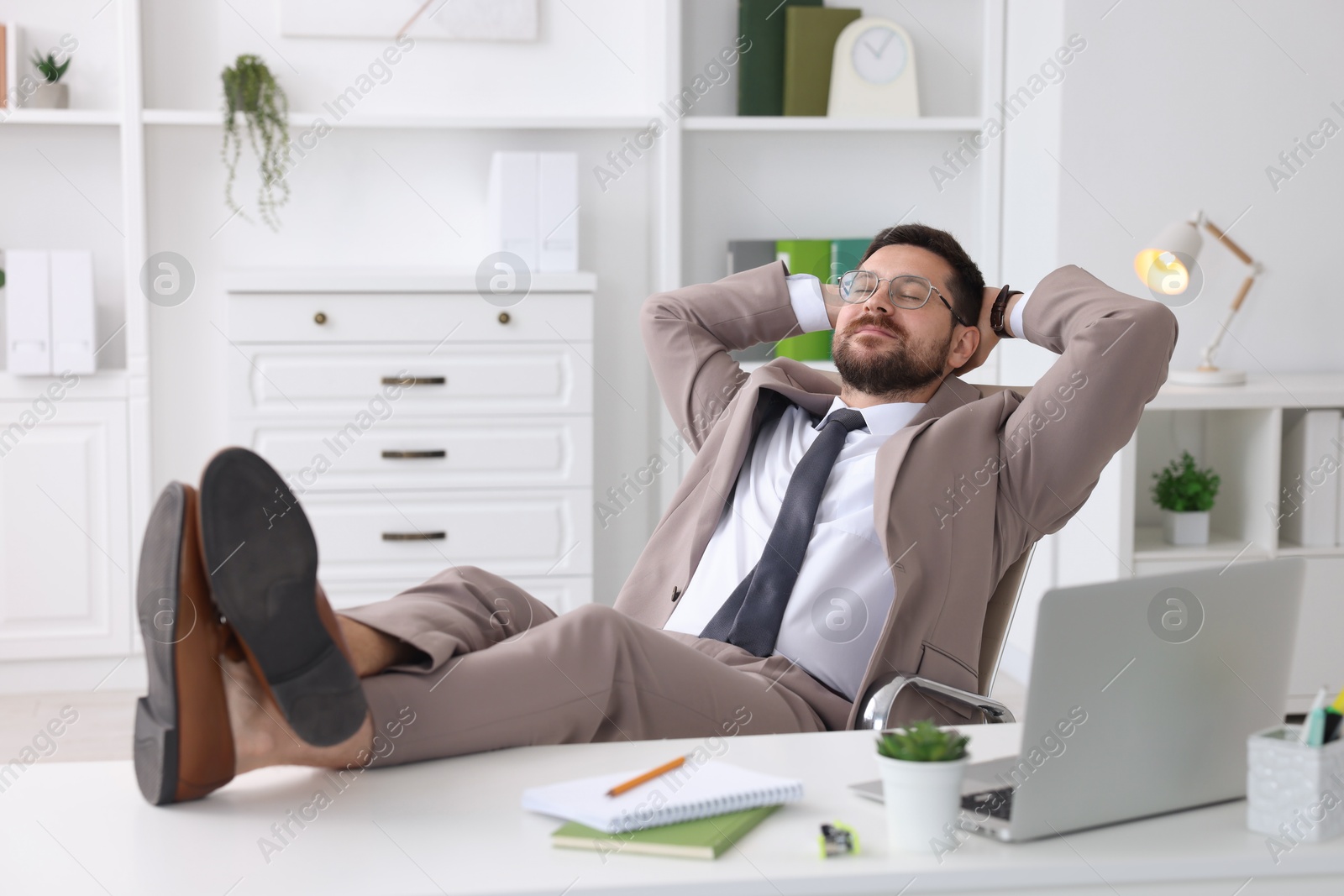 Photo of Businessman with hands behind his head holding legs on table in office. Break time