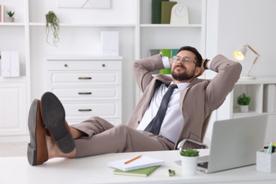 Businessman with hands behind his head holding legs on table in office. Break time