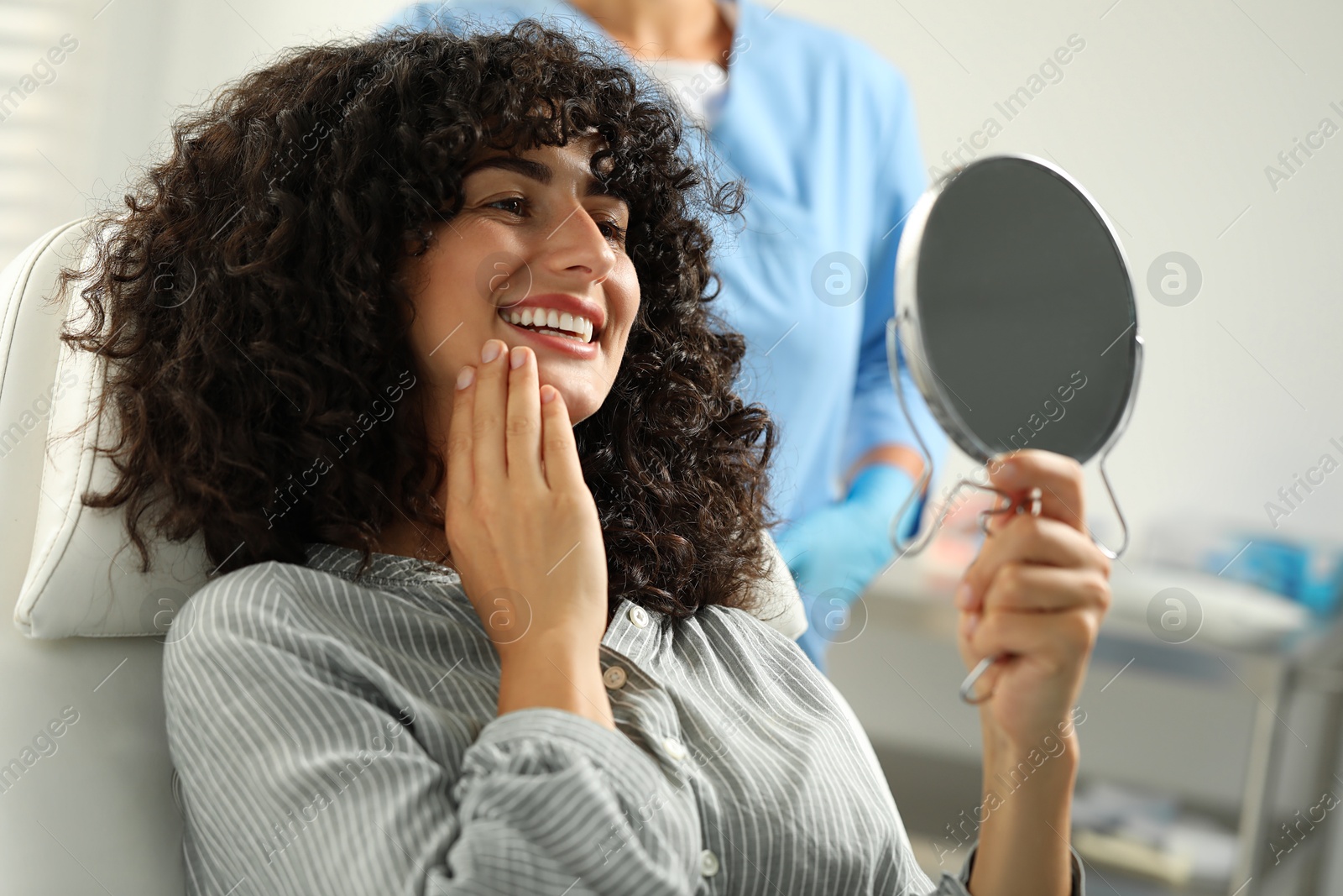 Photo of Patient looking in mirror and doctor in clinic, selective focus. Dental veneers