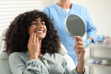 Photo of Patient looking in mirror and doctor in clinic, selective focus. Dental veneers