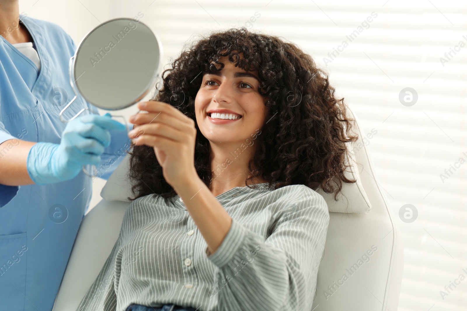 Photo of Patient looking in mirror and doctor in clinic. Dental veneers