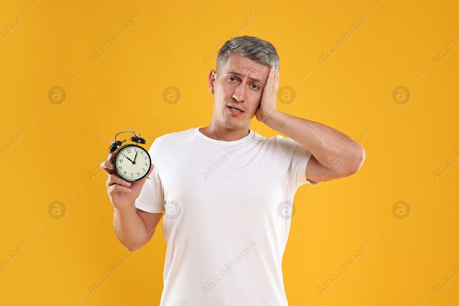 Photo of Overslept man with alarm clock on orange background