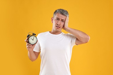 Photo of Overslept man with alarm clock on orange background