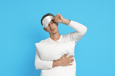 Photo of Overslept man with sleep mask and pillow on light blue background