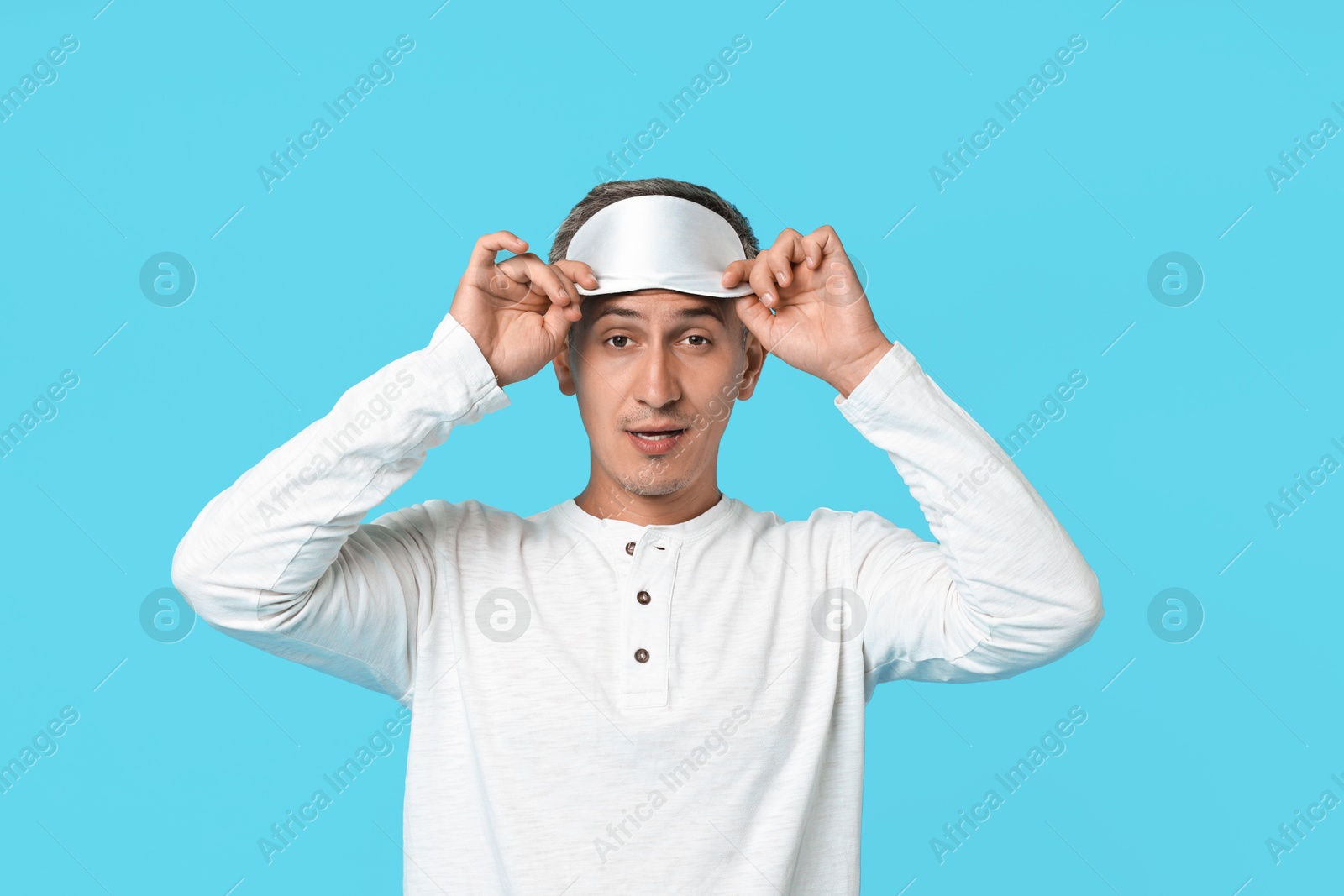 Photo of Overslept man with sleep mask on light blue background