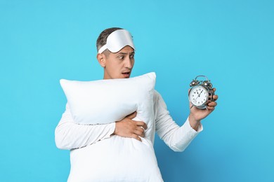 Overslept man with sleep mask, pillow and alarm clock on light blue background