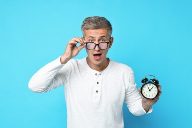 Overslept man in glasses with alarm clock on light blue background