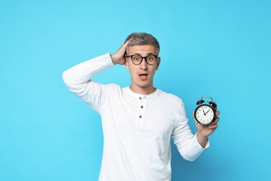 Overslept man in glasses with alarm clock on light blue background