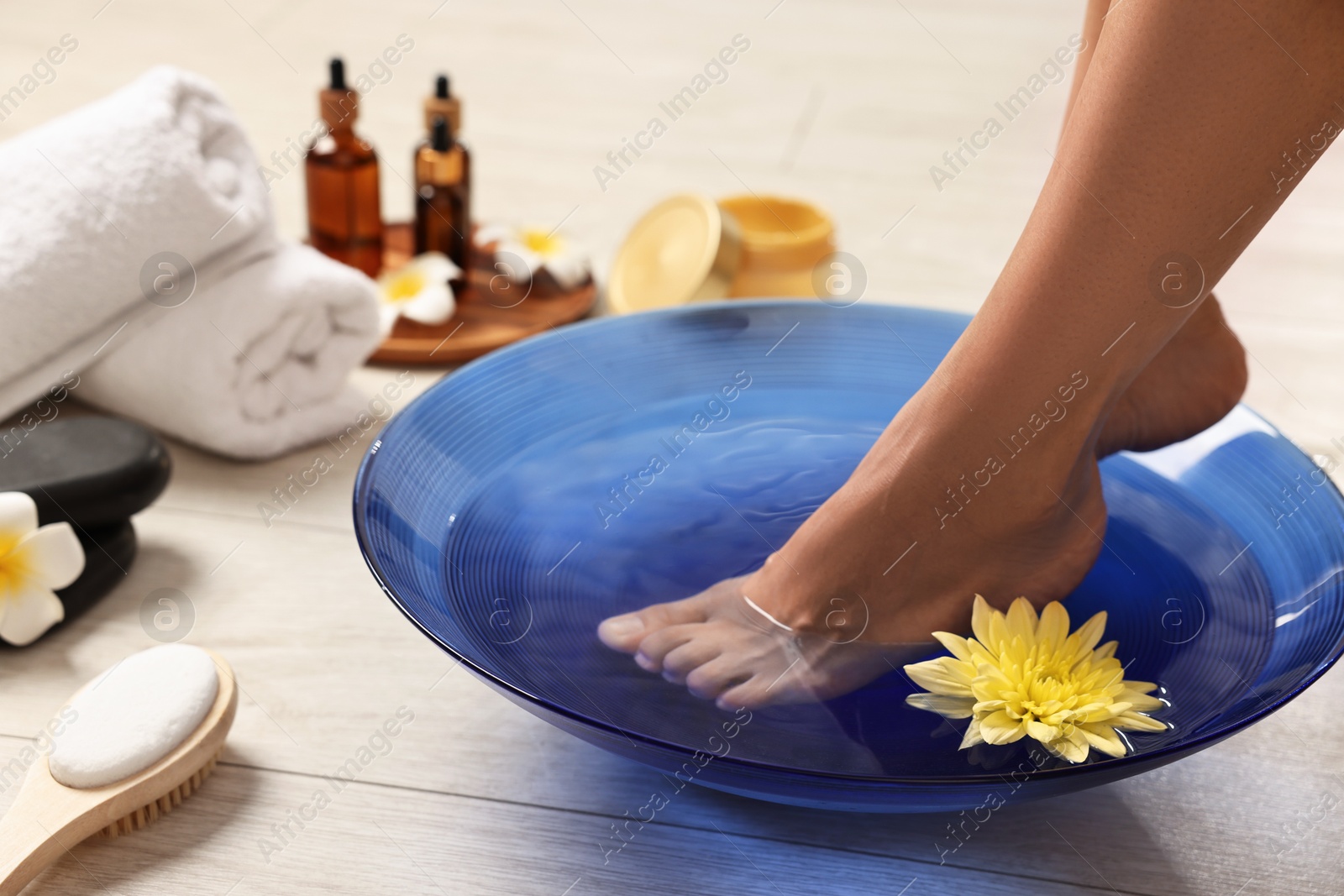 Photo of Woman soaking her feet in bowl with water and flowers on floor, closeup. Body care