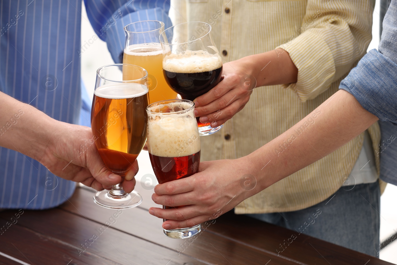 Photo of People with different types of beer clinking glasses at wooden table, closeup