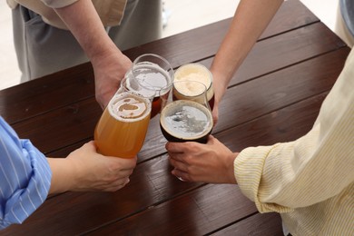 Photo of People with different types of beer clinking glasses at wooden table, closeup