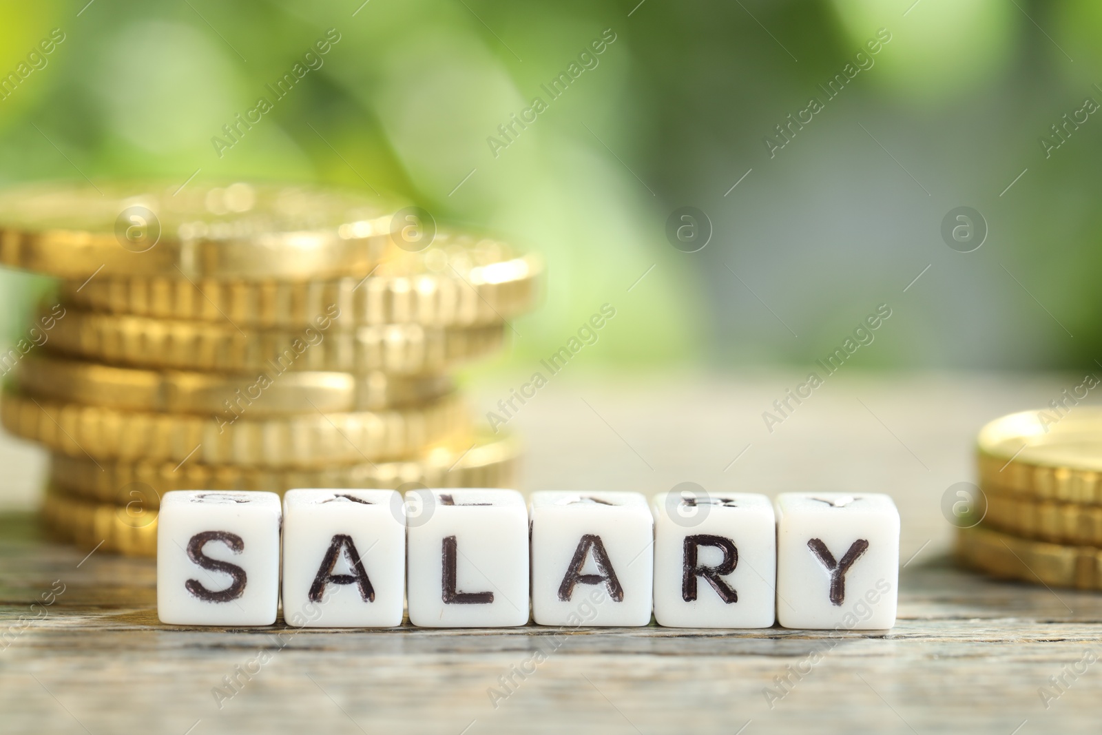 Photo of Word Salary made of cubes and coins on grey table against blurred background, closeup