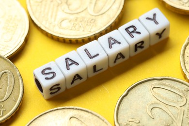 Word Salary made of cubes and coins on yellow background, closeup