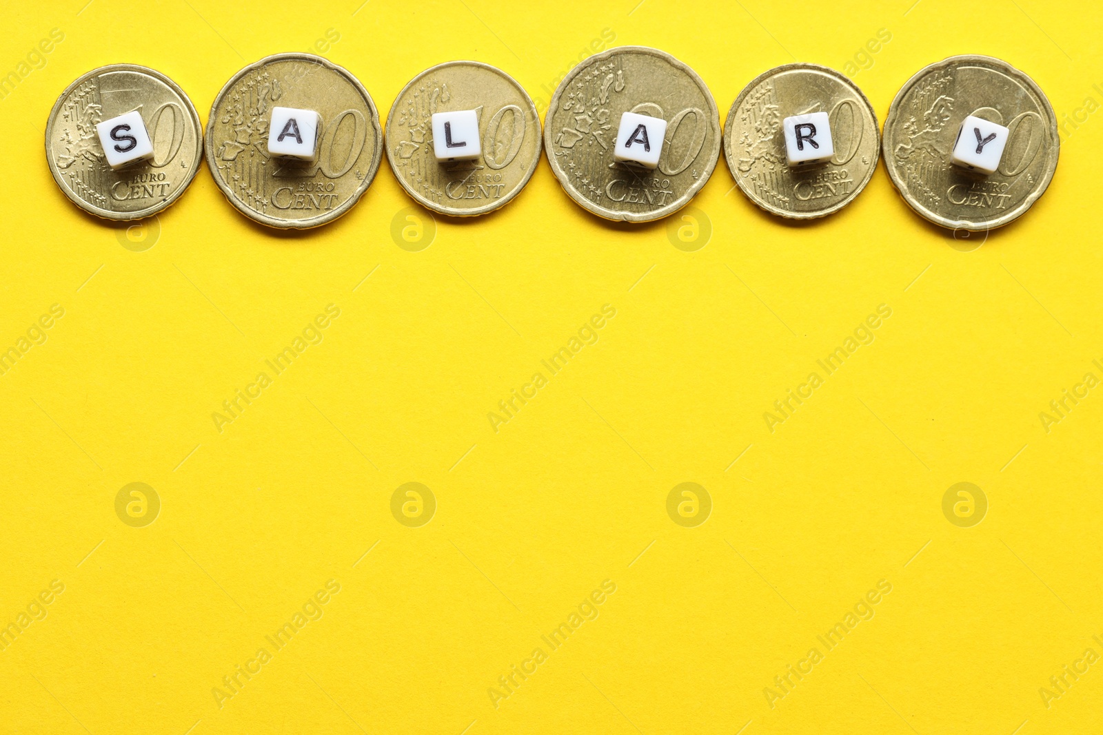 Photo of Word Salary made of cubes and coins on yellow background, flat lay. Space for text