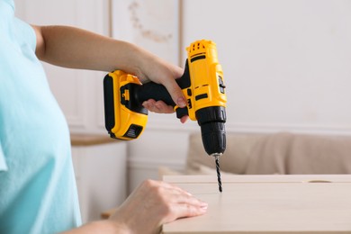 Photo of Woman with electric screwdriver assembling furniture at home, closeup