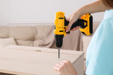 Woman with electric screwdriver assembling furniture at home, closeup