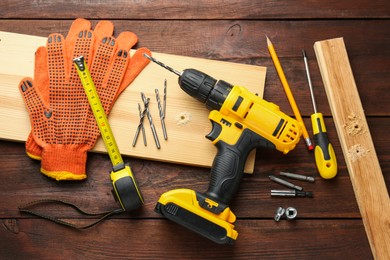 Cordless electric drill, gloves, pencil and construction tools on wooden table, flat lay