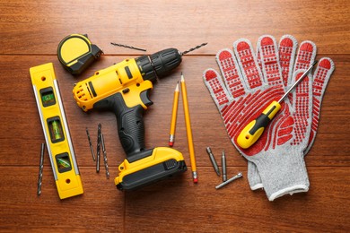 Photo of Cordless electric drill, gloves, pencils and construction tools on wooden table, flat lay