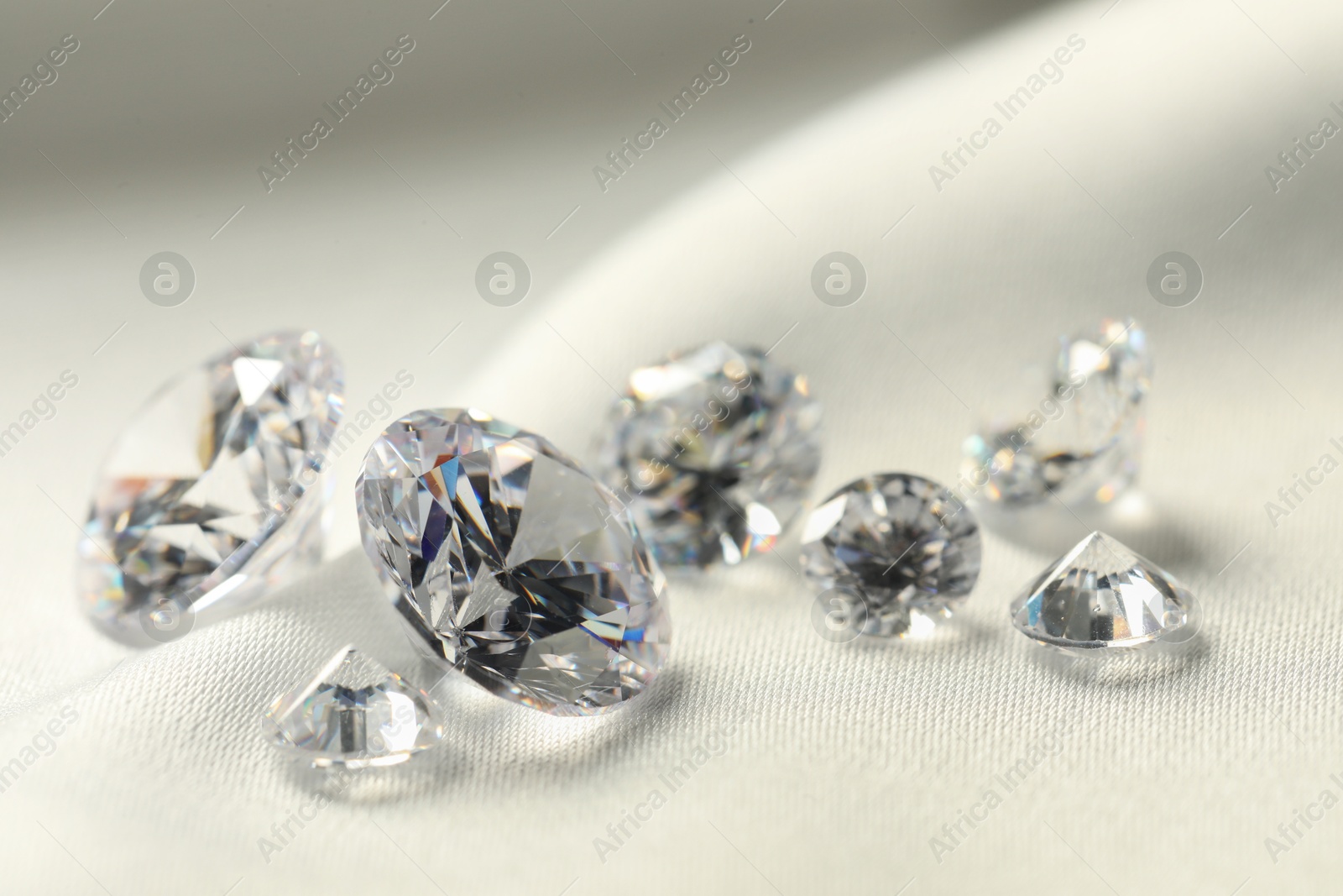 Photo of Many beautiful shiny diamonds on white fabric, closeup