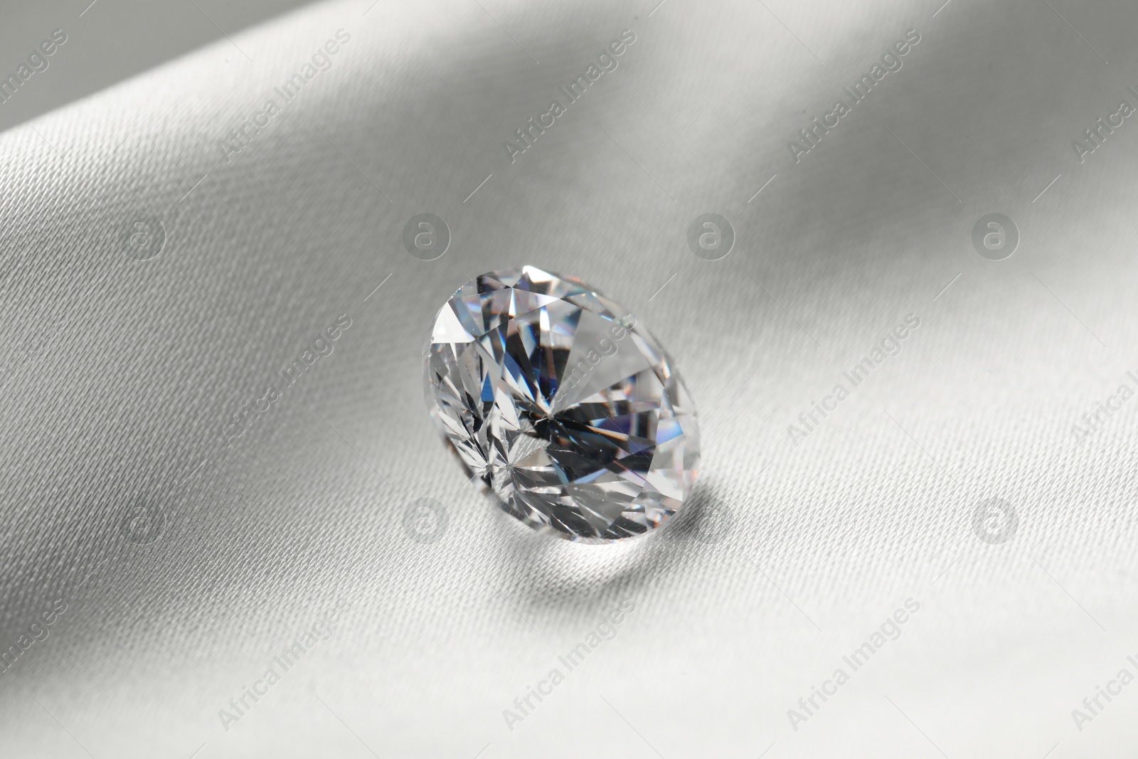 Photo of One beautiful shiny diamond on white fabric, closeup