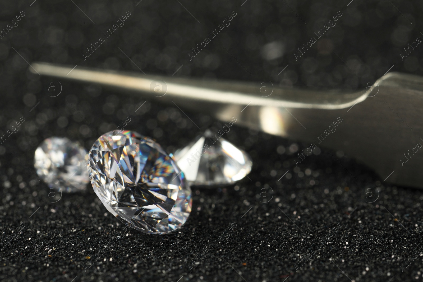 Photo of Beautiful dazzling diamonds and tweezers on dark shiny background, closeup