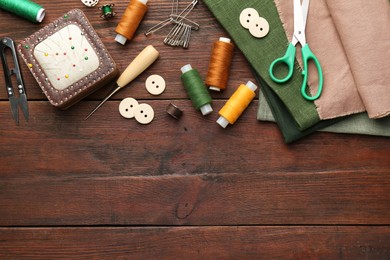 Flat lay composition with different sewing supplies on wooden table. Space for text