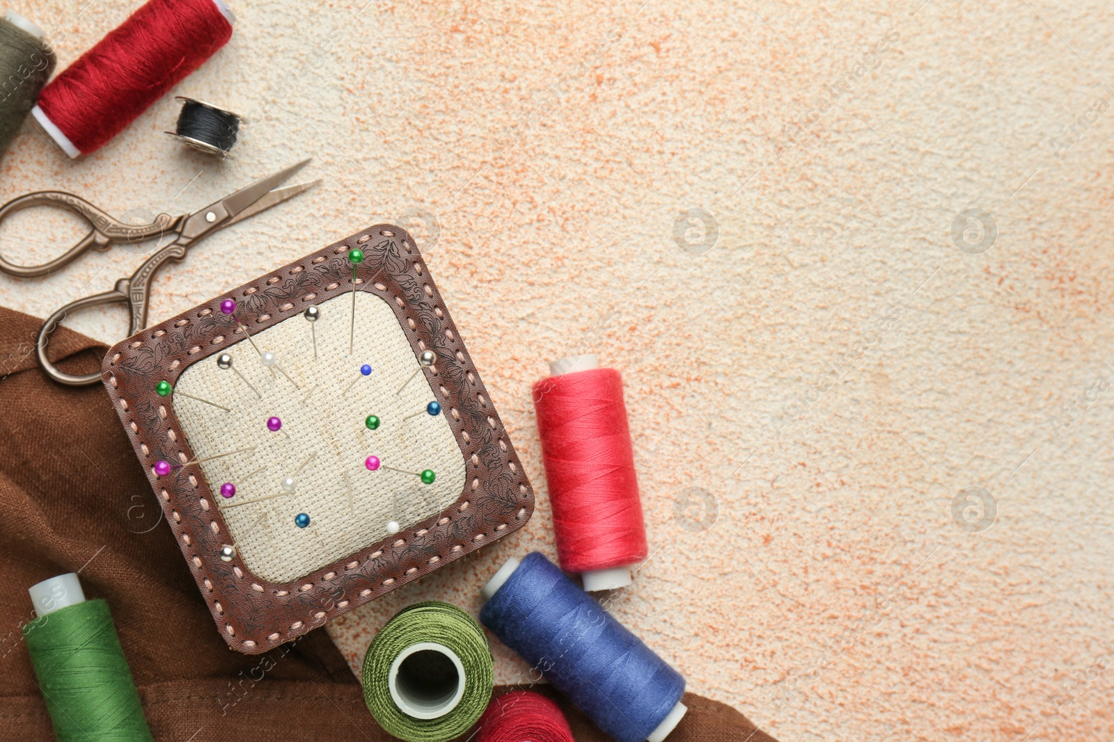 Photo of Flat lay composition with different sewing supplies on beige textured table. Space for text