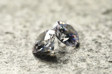 Photo of Two beautiful shiny diamond on grey textured table, closeup