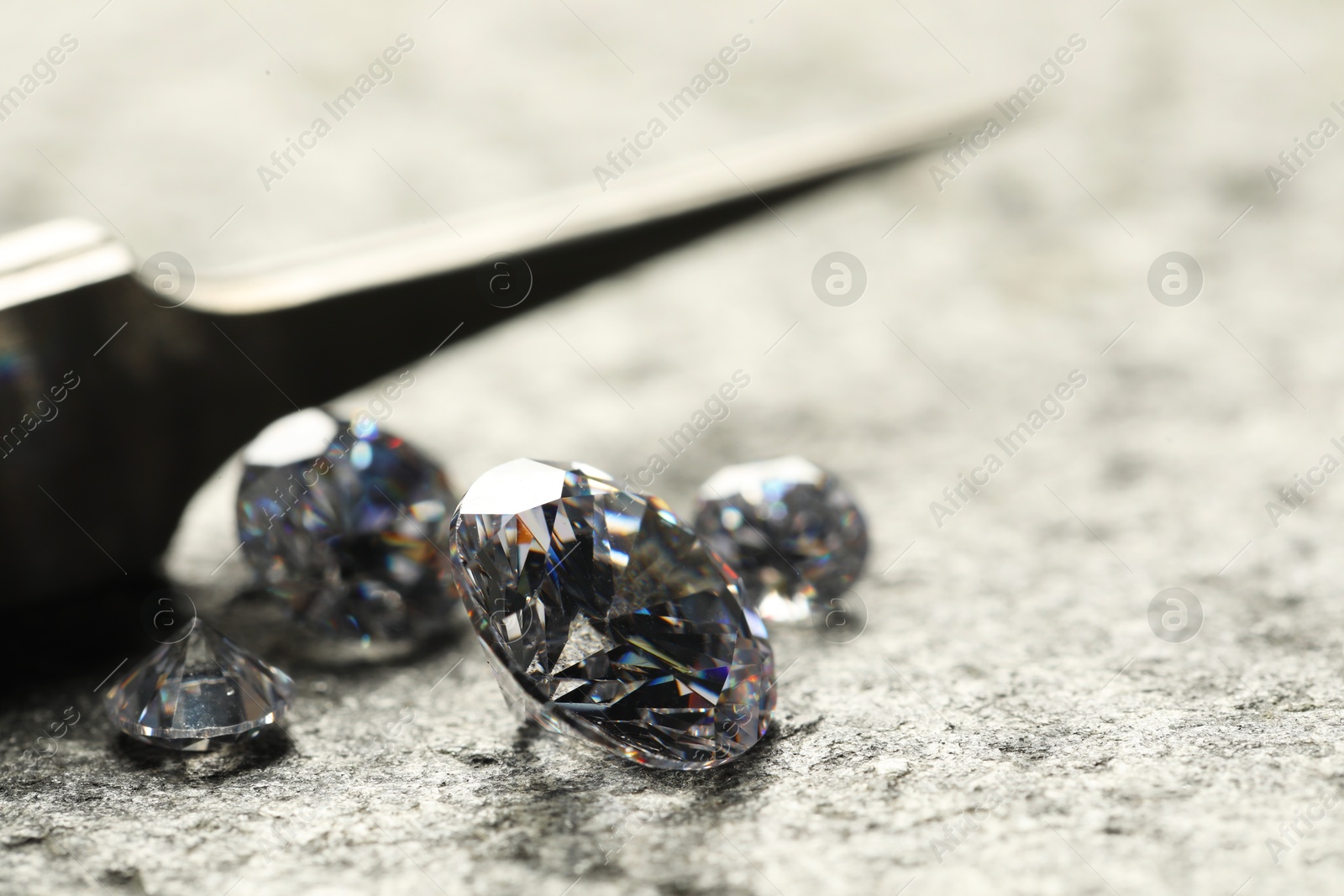 Photo of Many beautiful shiny diamonds and tweezers on grey textured table, closeup. Space for text